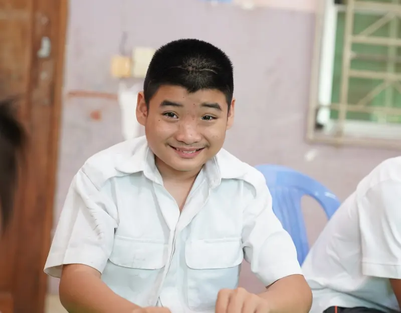 A boy in a white shirt smiles broadly at the camera.