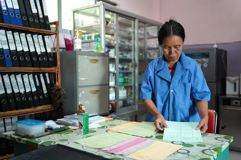 A carer in a blue uniform updates paperwork in the center's medical room.