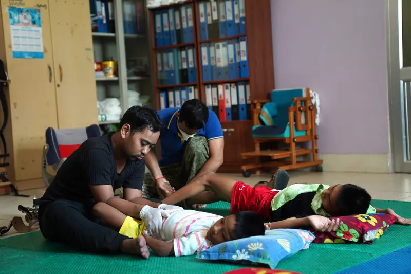 Two carers give physiotherapy to children lying on a green mat.