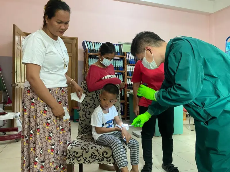 A doctor in green scrubs treats a child's foot while carers look on.
